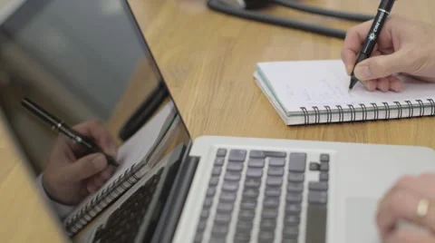 Businesman writing notes in the office, laptop in the foreground.  Stock Footage 68614581