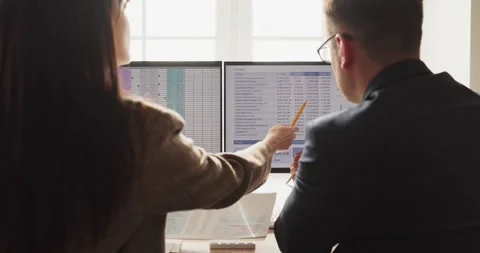 Business colleagues analyzing financial data on dual computer monitors in office Stock Footage 337014888