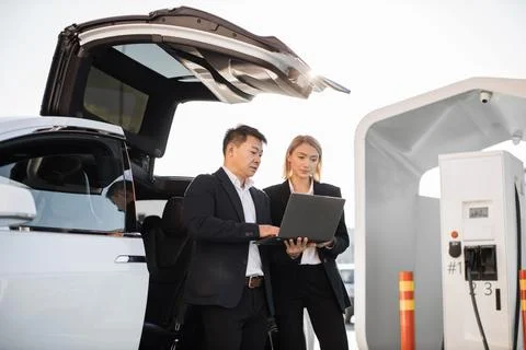 Business colleagues using laptop while charging electric car 스톡 사진