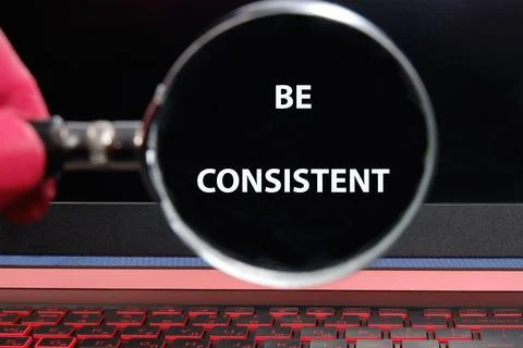 Business concept text BE CONSISTENT through a magnifying glass on a laptop .. Stockfoto's