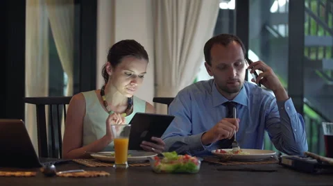 Business couple with cellphone, tablet computer and laptop eating dinner HD Stock Footage 42311599