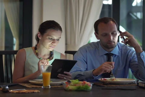 Business couple with cellphone, tablet computer and laptop eating dinner NTSC Stock Footage 42311604