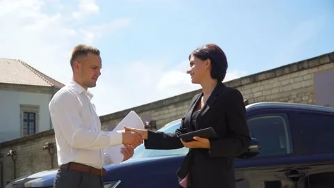 Business couple with documents and tablet near the car shake hands. People and Stock Footage 136593606
