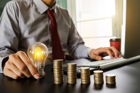 Business hand holding lightbulb with using laptop computer and money stack .. Stock Photos