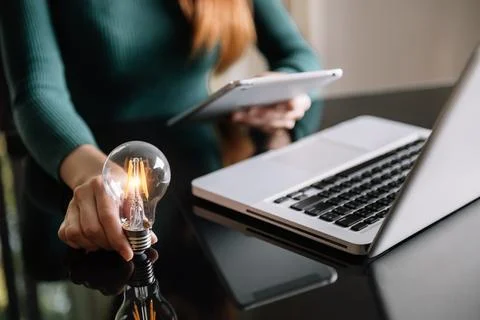 Business hand holding lightbulb with using laptop computer and money stack .. Stock Photos
