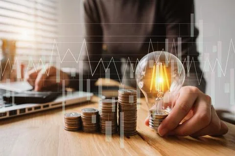 Business hand holding lightbulb with using laptop computer and money stack .. Stock Photos