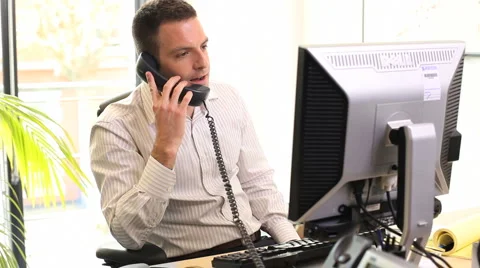 Business male talking on phone in office and looking at computer screen Stock Footage