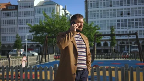 A business man with a beard in a coat talks on the phone in sunny weather Stock Footage 220320761