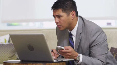 Business man in office lobby using laptop and cell phone Stock Footage