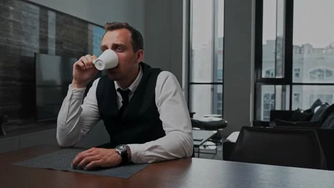 Business man sitting at the table in the office, drinks coffee from a white cup Stock Footage 201199977