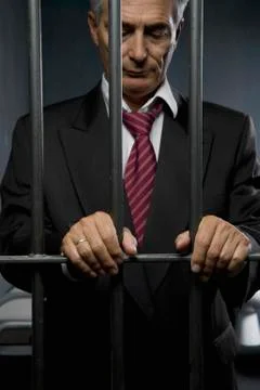 A business man standing behind prison cell bars Stock Photos