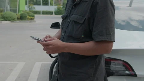 Business man use smartphone to use ev car charge outdoor station Stock Footage 253405752