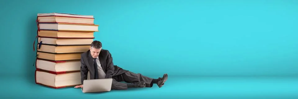 Business man using computer on the floor next to a pile of books on blue Foto stock
