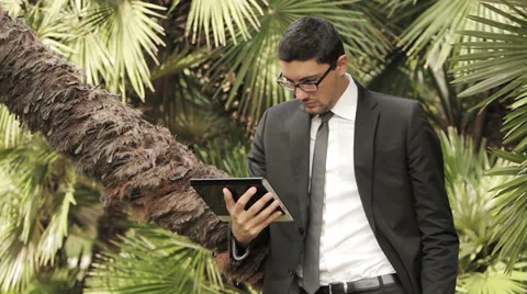 Business man using a digital tablet device while standing in a classic park Stock Footage 32579138