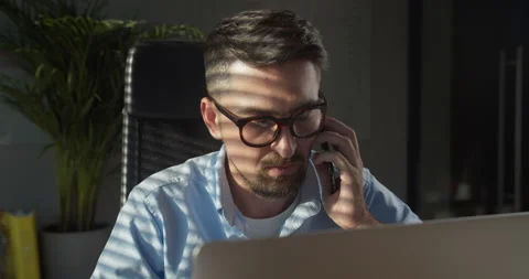 Business man using laptop talking on cell phone sits at desk. confident male Stock Footage 157735060