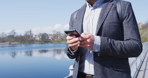 Business man Using Smart Phone Wearing Suit By Lake In City Park On Sunny Day Stock Footage 102475418
