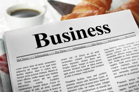 Business in newspaper layout on a breakfast table with a blurry cup of coff.. Stock Photos