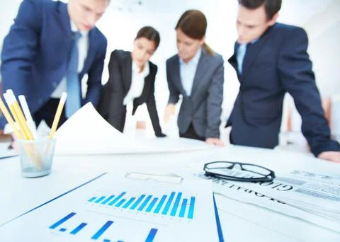 Business objects on background of engineers discussing blueprint at meeting Stock Photos