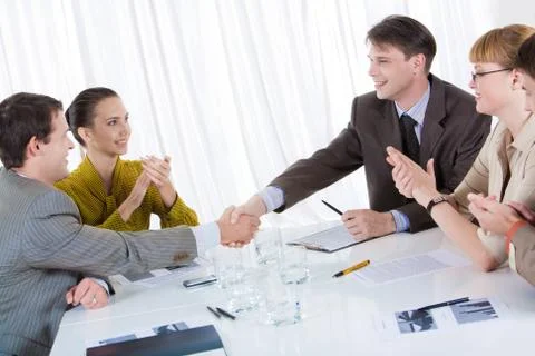 Business partners shaking hands after striking deal while their co-workers appla Stock Photos