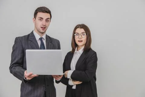 Business partners standing, checking data in the laptop, looking at the camera Stock Photos