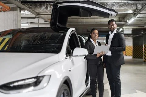 Business partners viewing data on device by e-car in garage Stock Photos