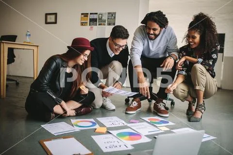 Business people discussing plans sitting on floor with papers and laptop Stock Photos