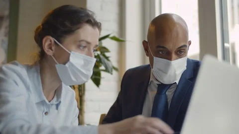 Business people with face masks working together on laptop in modern coworking Stock Footage