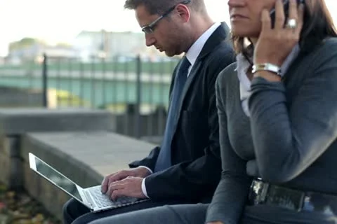 Business people sitting in the city with cellphone and laptop, steadycam shot Stock Footage
