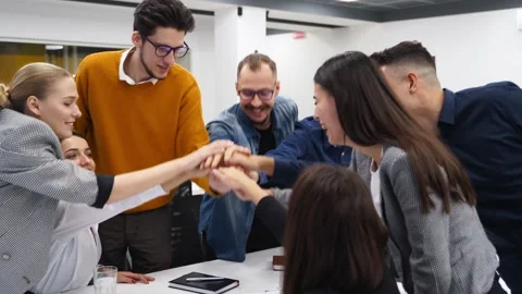 Business people stack hands in pile over meeting table, cheer together in Stock Footage 195934111