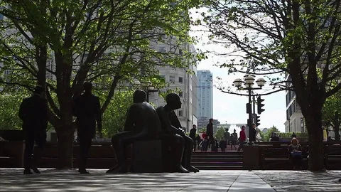 Business people walk through a leafy square at Canary Wharf on a sunny day Stock Footage