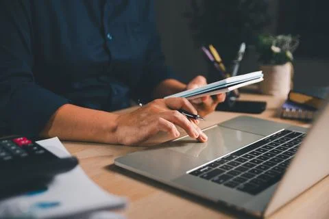 Business professional holding a notebook while using a laptop at a modern w.. Stock Photos