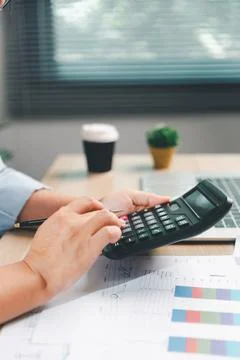 Business professional using a calculator over financial reports beside a la.. 스톡 사진