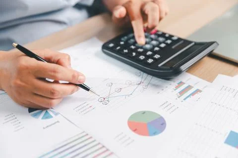 Business professional using a calculator while pointing at printed charts w.. Stock Photos