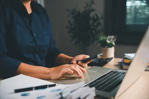 Business professional using a smartphone while working on a laptop with fin.. Stock Photos