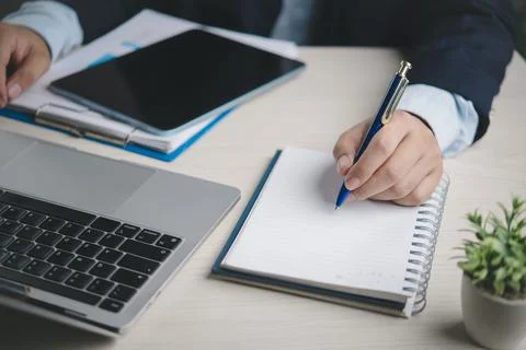 Business professional writes notes on notebook at office desk with laptop t.. 写真素材