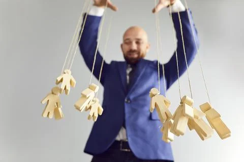 Business puppet master playing with human figures illustrating concept of Stock Photos