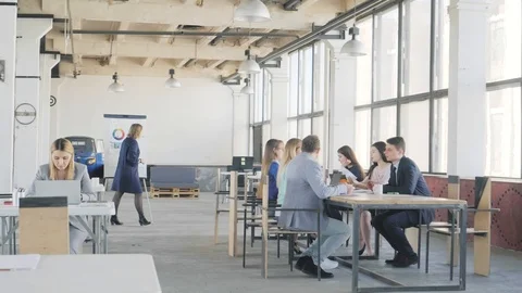 The business team at the big table holds a meeting. Nearby, a colleague finishes Stock Footage 109557235