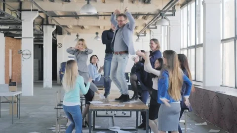 A business team cheerfully dances while standing on a table in an office Stock Footage 111657643