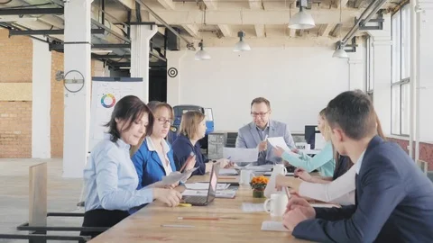 A business team is sitting at a large table in a creative office space and is Stock Footage 109418715
