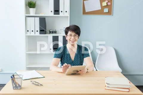 Business, technology and people concept - middle aged woman sit at the table and Stock Photos
