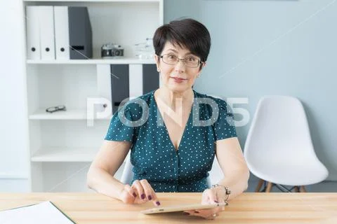 Business, technology and people concept - middle aged woman sit at the table and Stock Photos