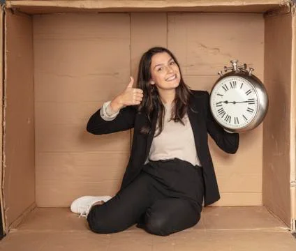 Business woman with a clock in hand sits in a cardboard office Stock Photos