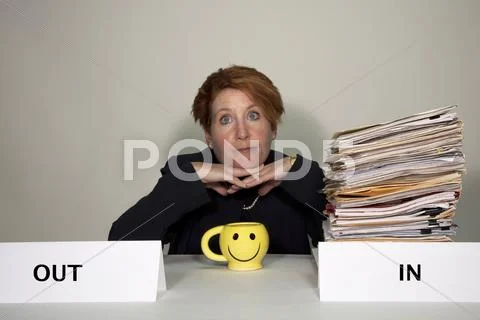 Business woman sitting at a desk with an overflowing in box dreaming of quitt Stock Photos