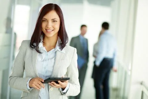 Business woman standing in foreground with a tablet in her hands, her co-workers Stock Photos