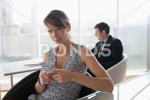 Business woman using mobile phone, male colleague in background Stock Photos