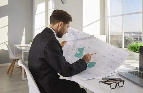 Businessman analyzing cadastral map while sitting at desk in office Stock Photos