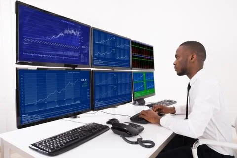 Businessman Analyzing Data Displayed On Multiple Computer Screens In Office Foto stock