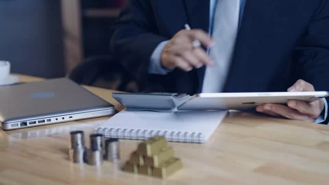 Businessman analyzing financial data on tablet with calculator, gold bars, .. Stock Footage 328440316