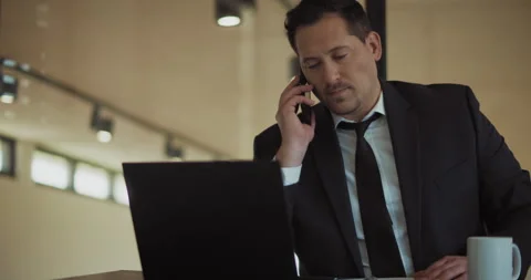 A businessman answering a phone while working on a computer at the office. Stock Footage 140207581