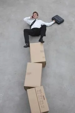 Businessman balancing on stack of cardboard boxes, using mobile phone, elevated Stock Photos